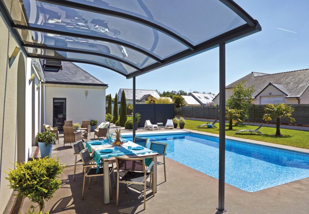 Une table et des chaises sont abritées sous un toit terrasse design à côté de la piscine