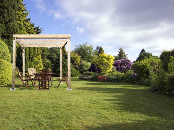 une pergola en bois clair au milieu d'un grand jardin